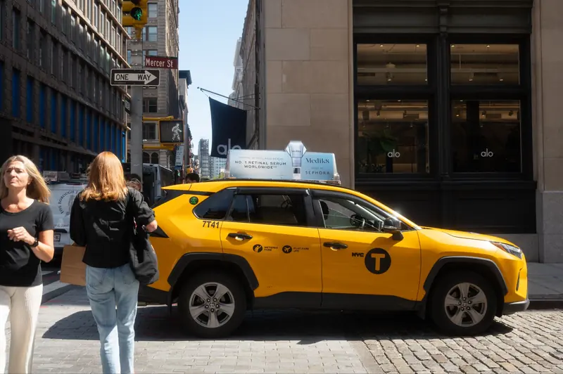 A yellow cab with a custom static top on a Midtown street