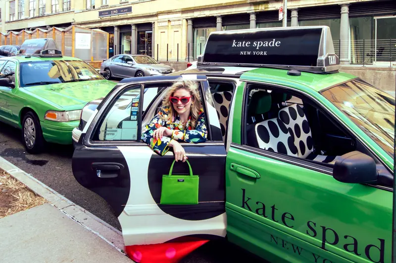 A model steps out of a green cab carrying a fashion brand's static top