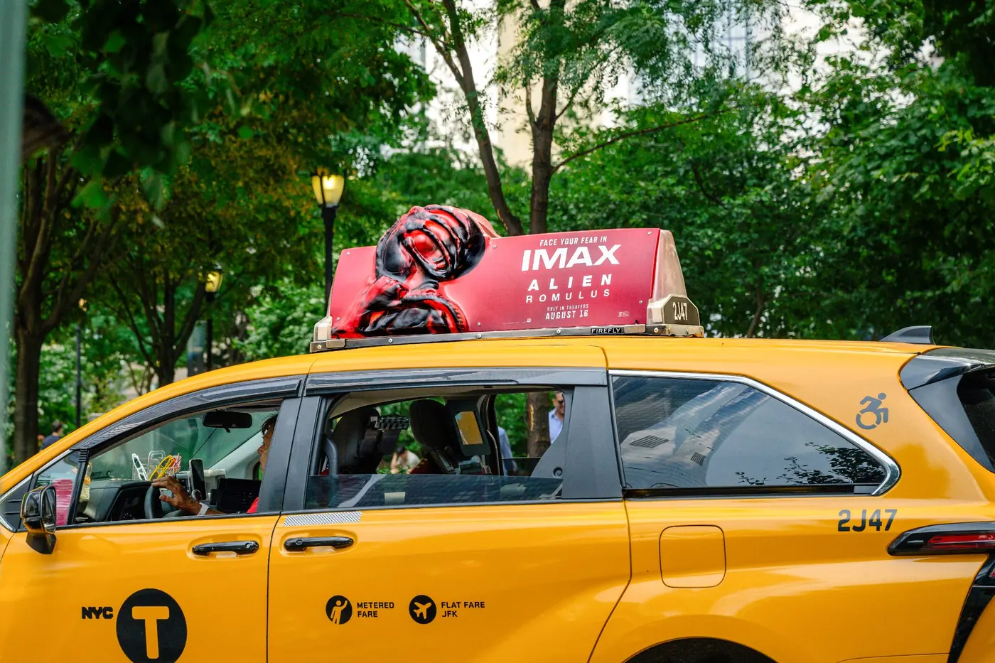 A fully dimensional Firefly Icon Sculpt top on a yellow cab passing through a tree-lined street