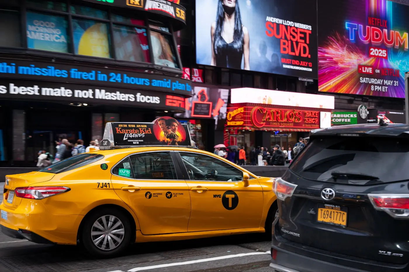 A yellow cab with a static top driving through Times Square traffic